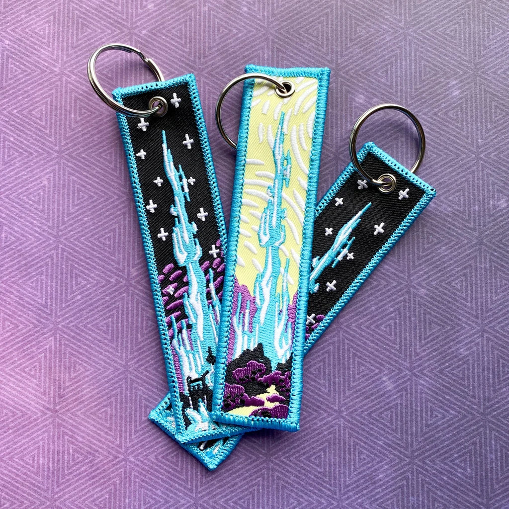 Three embroidered keychains with Crystal Tower design on a purple patterned background