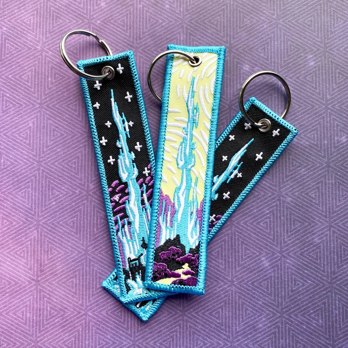 Three embroidered keychains with Crystal Tower design on a purple patterned background
